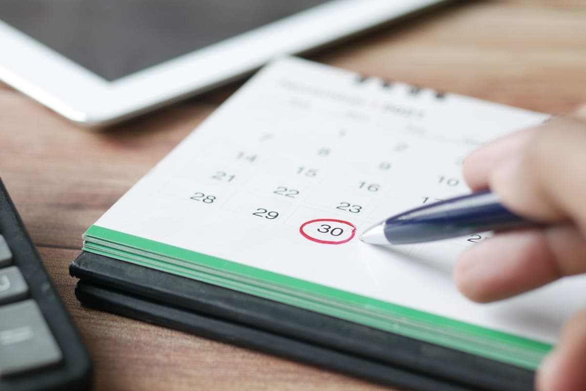 A hand marking a date on a paper calendar with a pen