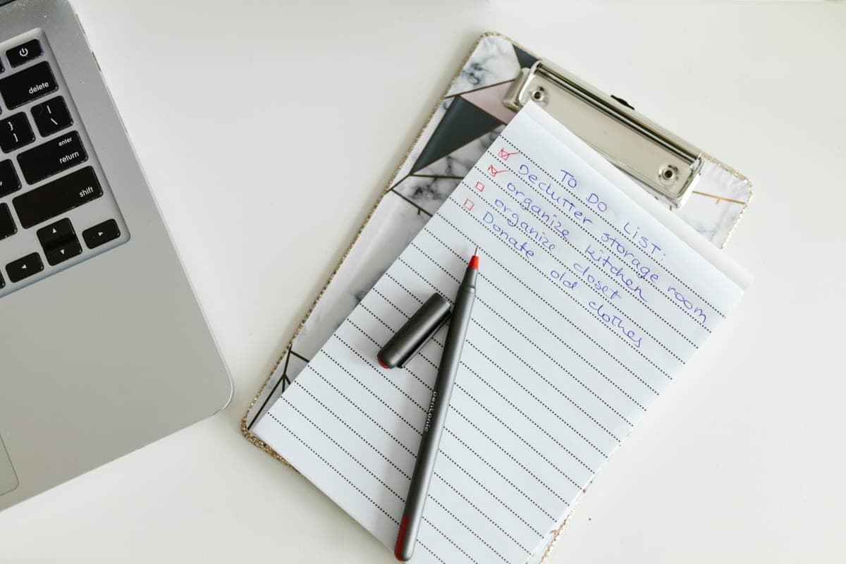 A checklist on a clipboard beside a laptop and a pen