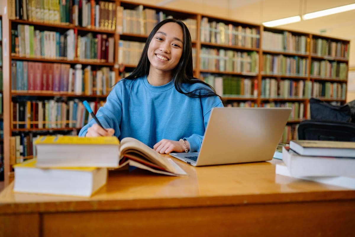 A student working with books and a laptop at a library table