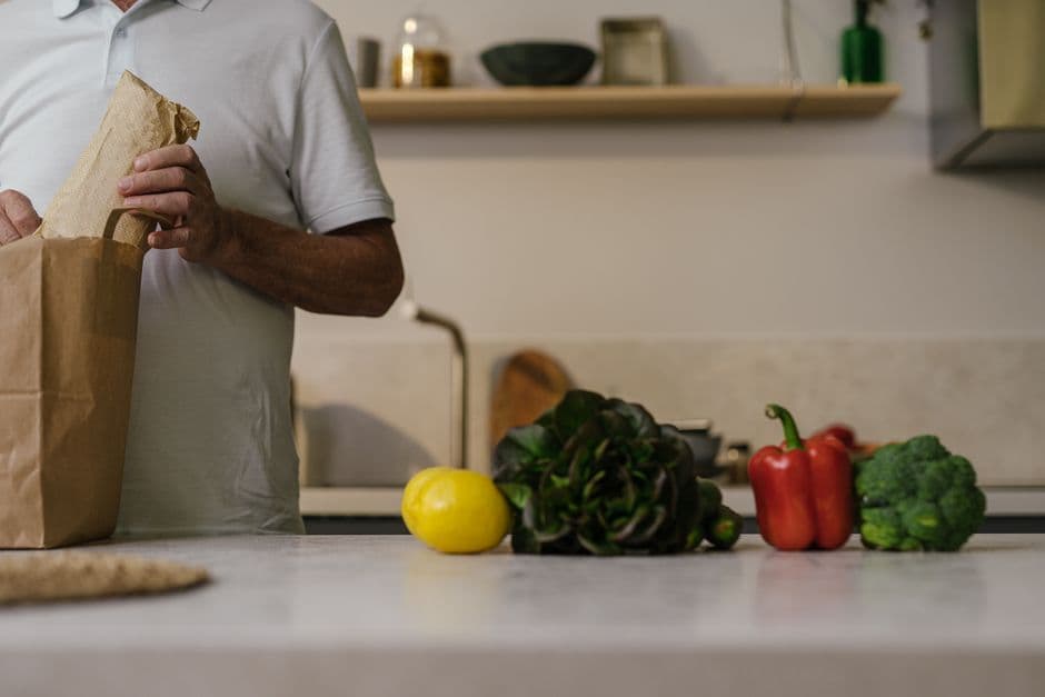 A man unpacking fresh vegetables from a paper grocery bag