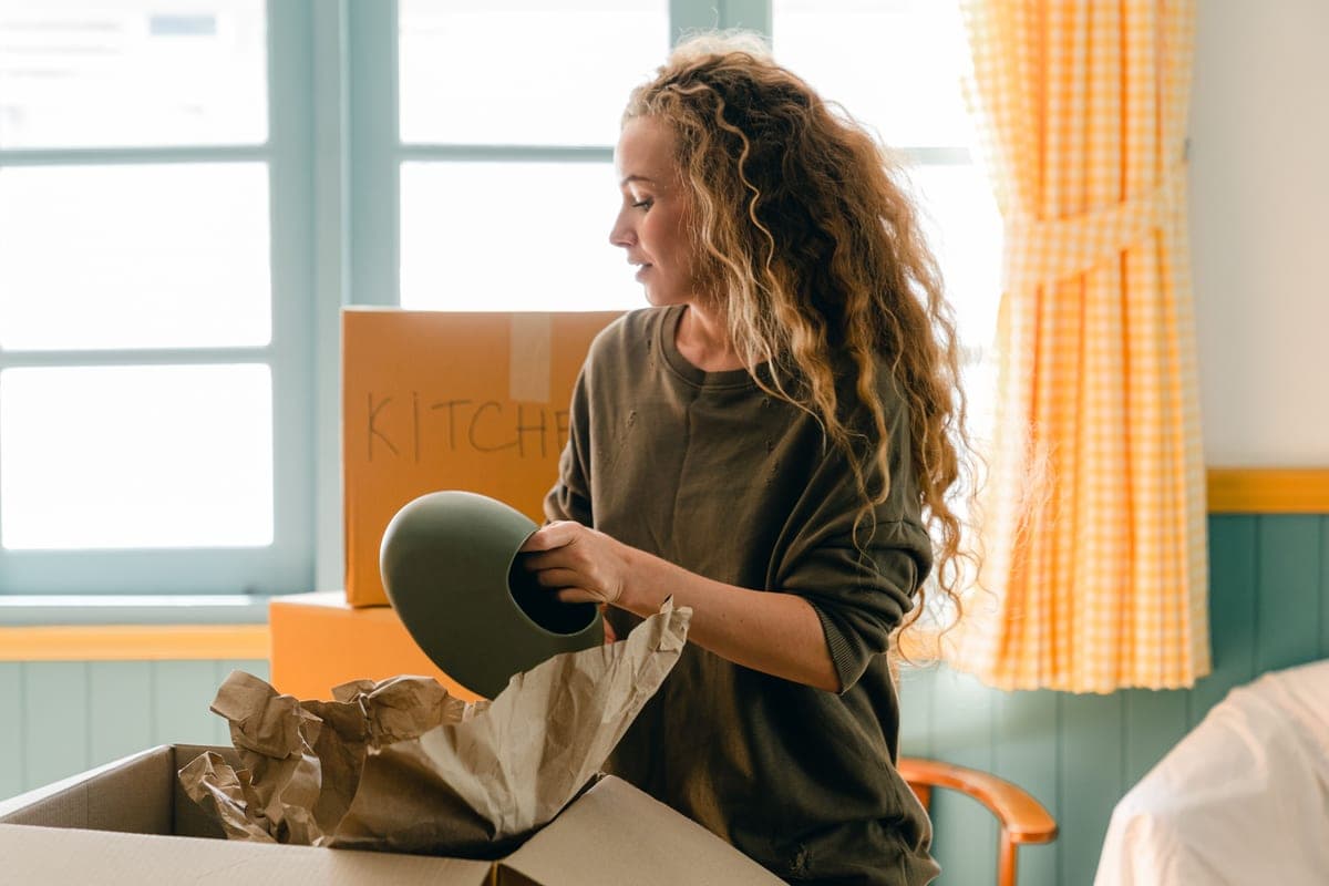 A person unpacking an item from a cardboard box beside a stack of boxes