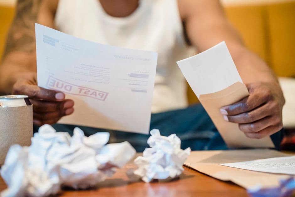 A person reviewing bills and crumpled paperwork on a coffee table