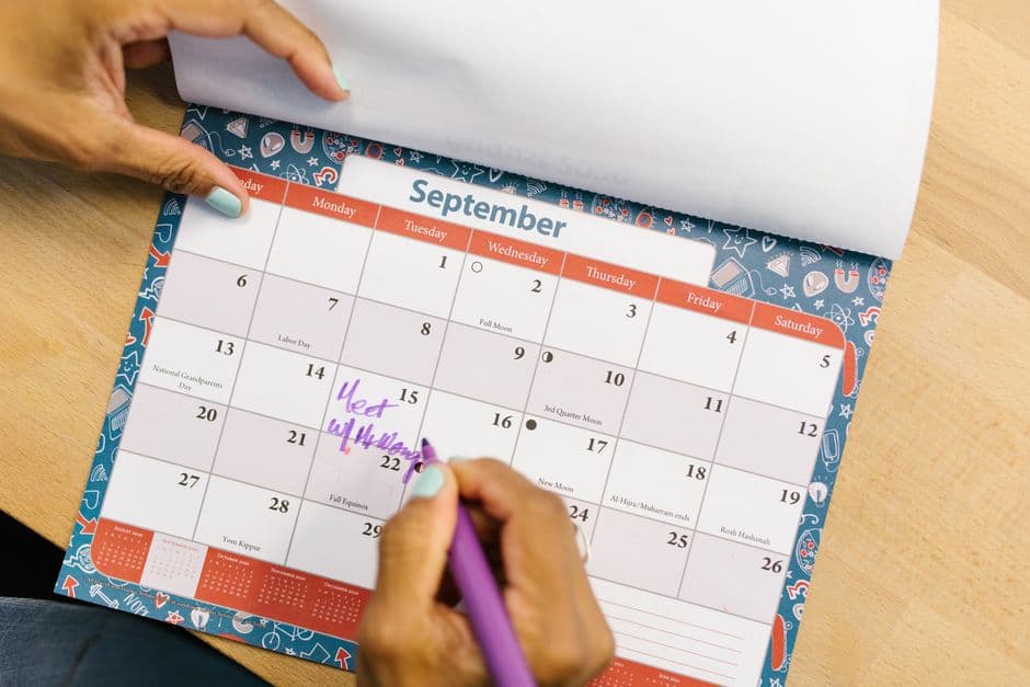 A person marking a date on a paper calendar with a pen