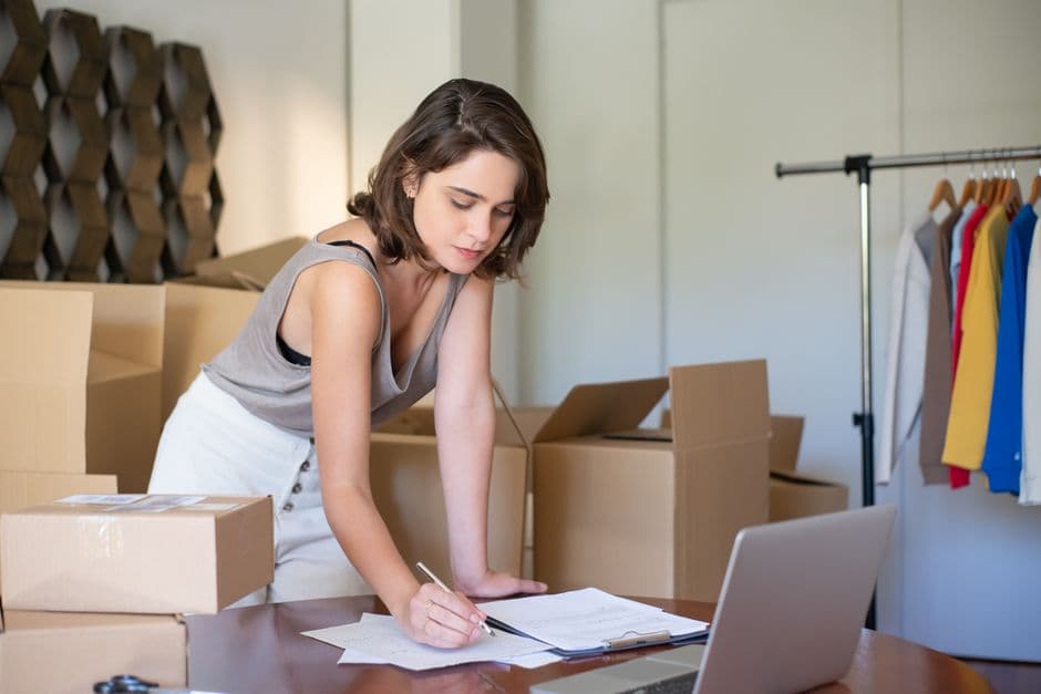 A small business owner packing orders beside a laptop and cardboard boxes