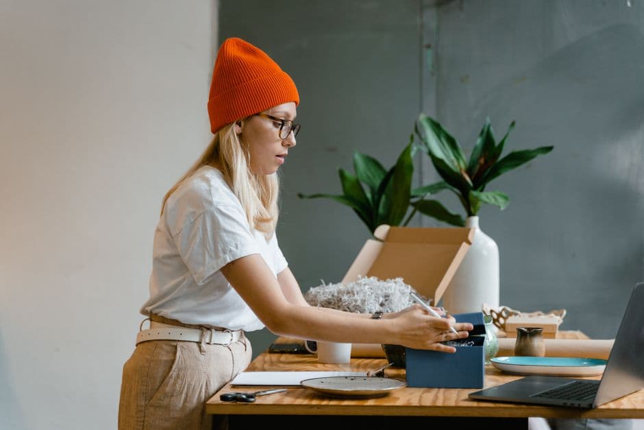 A woman packing an item into a box at a wooden table