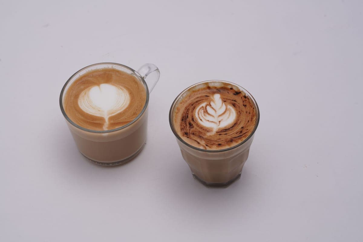 Two glass cups of latte side by side on a white surface