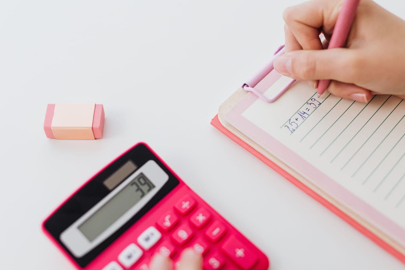 Hands using a calculator and writing figures in a notebook