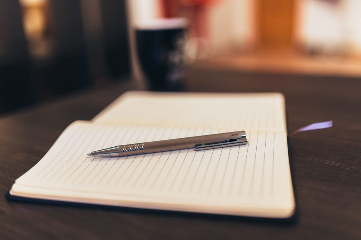 An open notebook and pen on a table with a mug behind