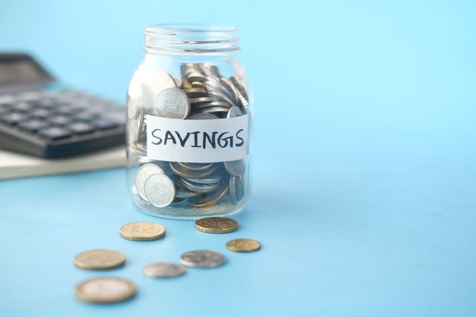 A glass savings jar filled with coins beside a calculator
