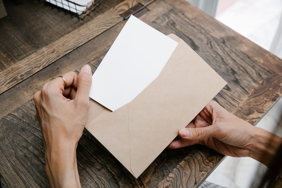 Hands holding a letter taken from a brown envelope on a wooden desk