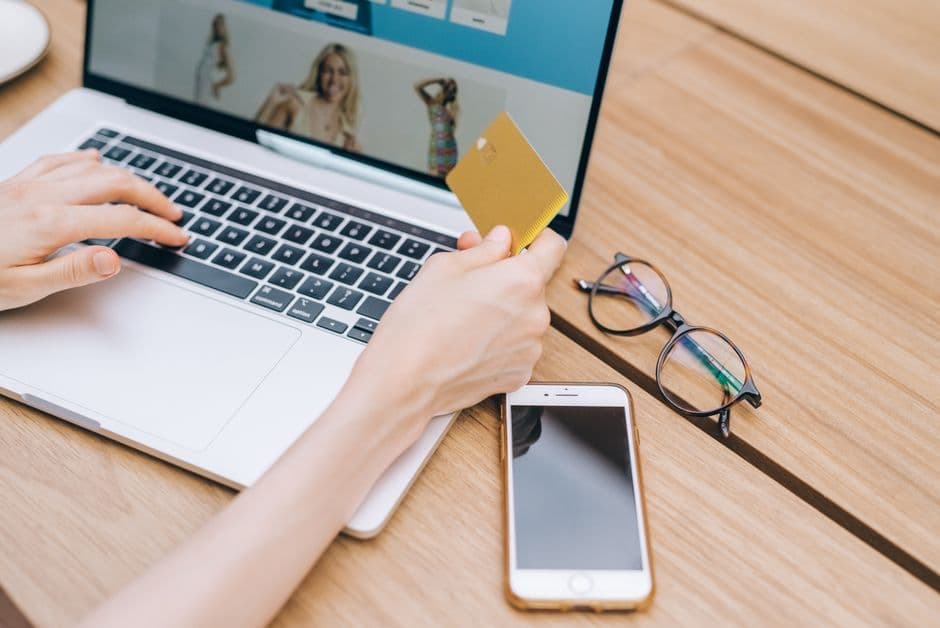 A person making an online purchase with a card, laptop and phone