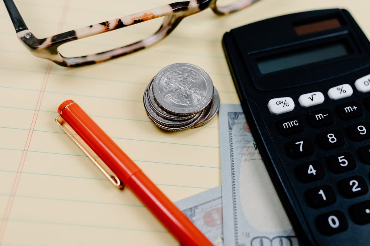 A calculator, coins and reading glasses on a notepad