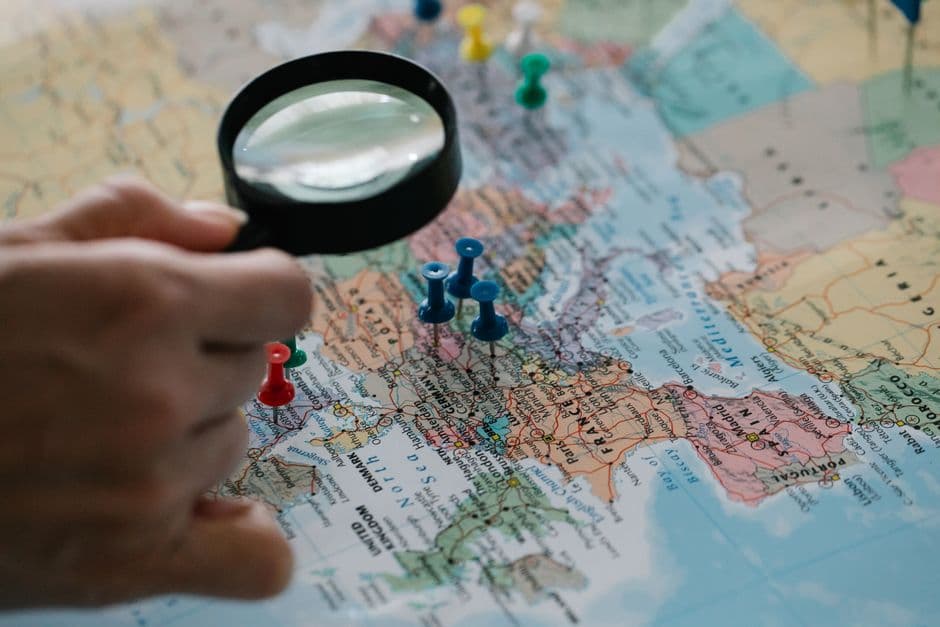 A hand holding a magnifying glass over a pinned map