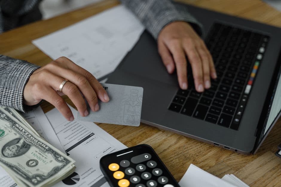 A hand holding a card while using a laptop