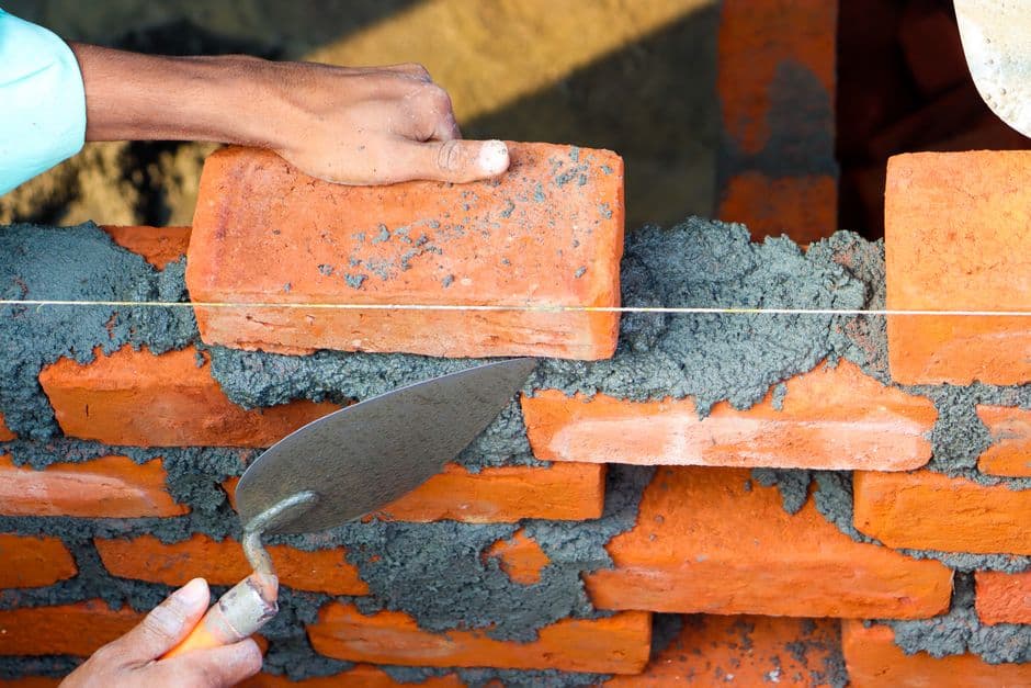 Hands laying bricks and mortar on a wall