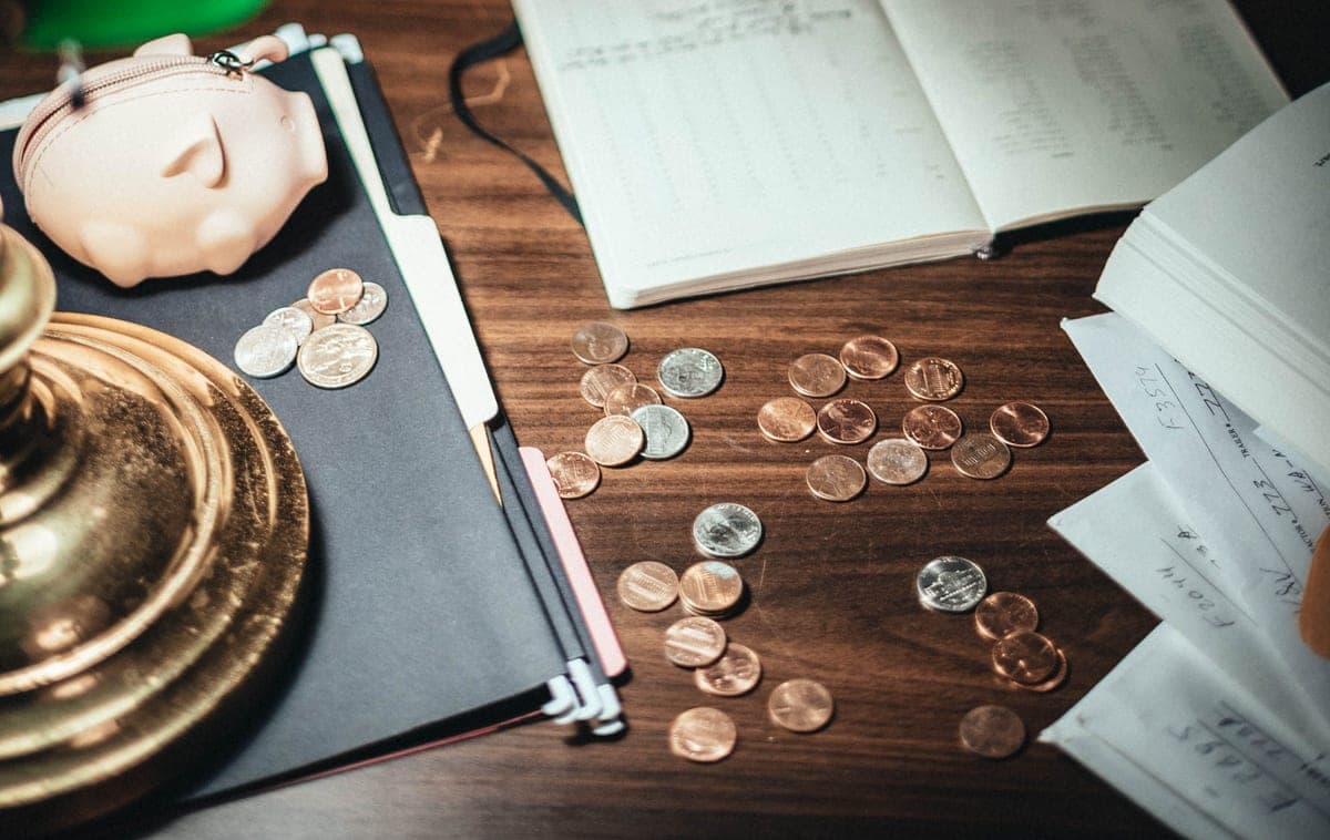 Coins scattered on a desk beside financial paperwork and a piggy-bank wallet